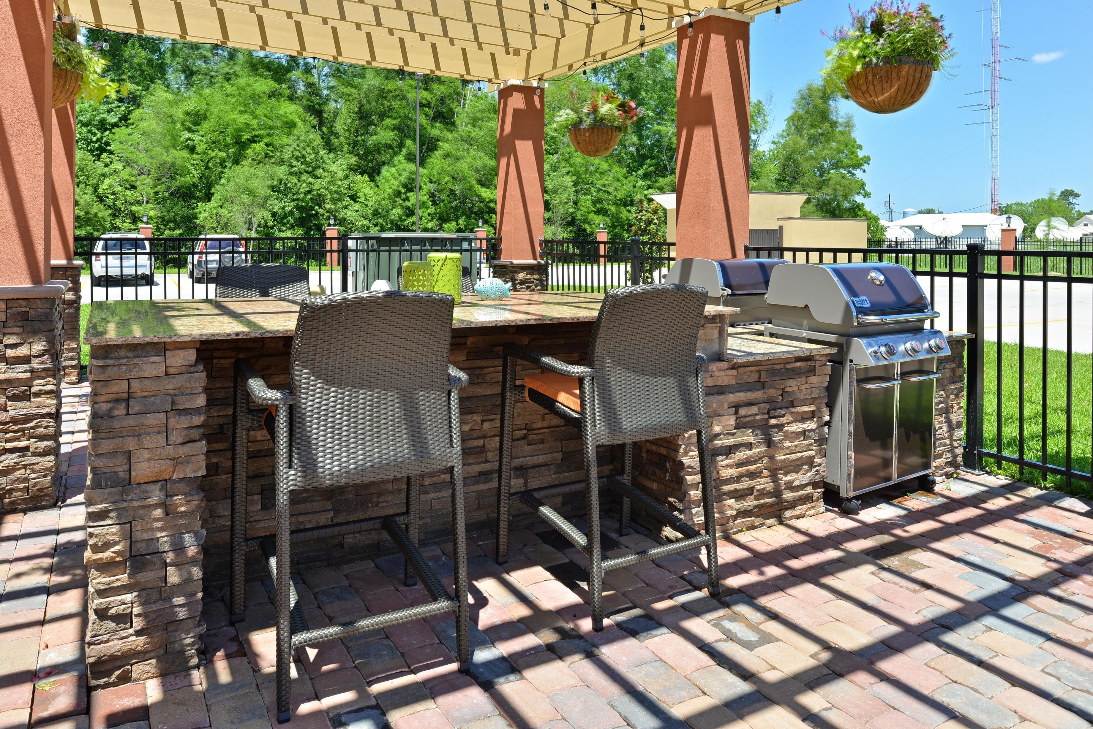 An outdoor patio with a grill and two wicker chairs.