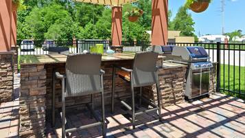 An outdoor patio with a grill and two wicker chairs.