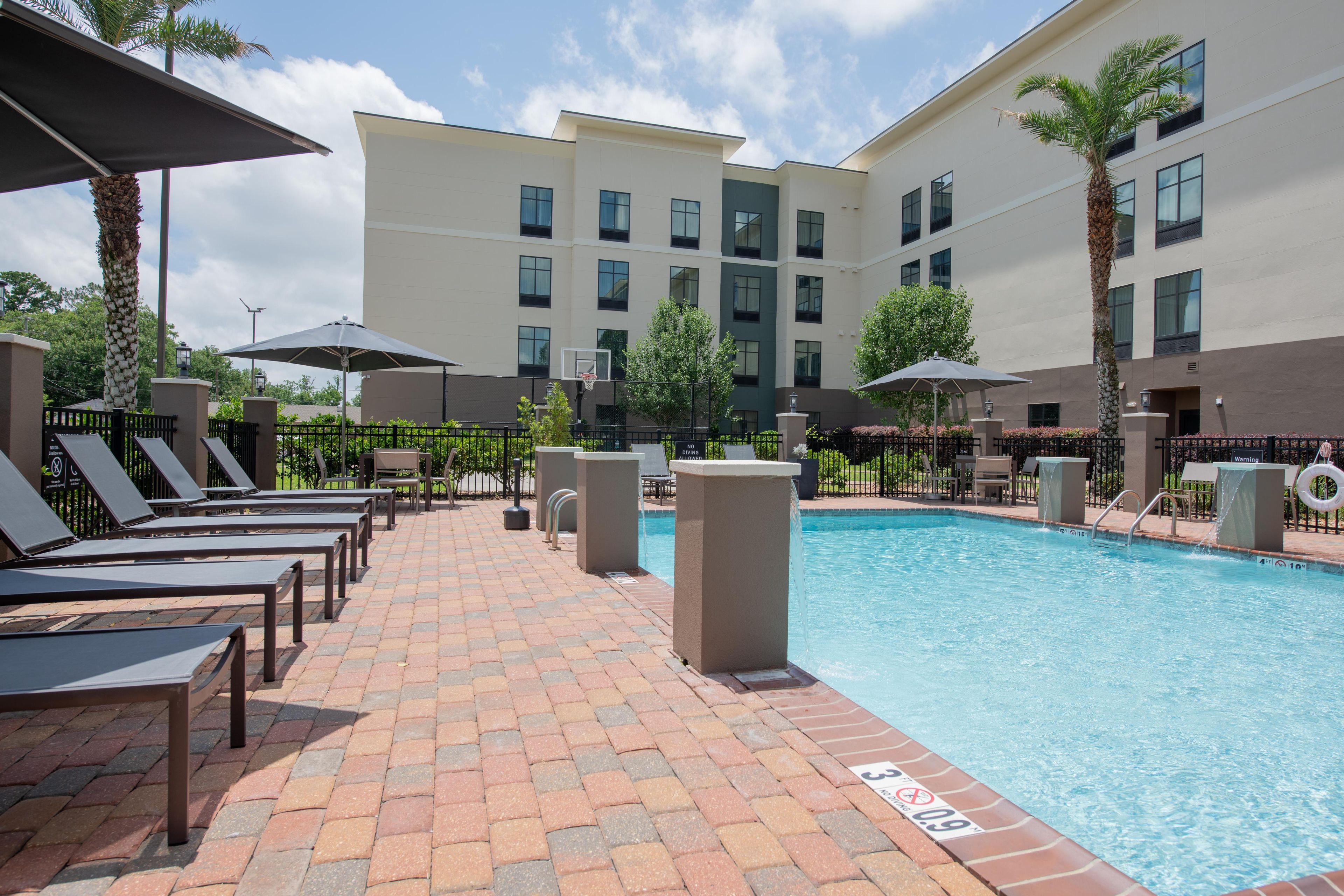 A pool area with lounge chairs, a diving board, and a building with multiple windows.