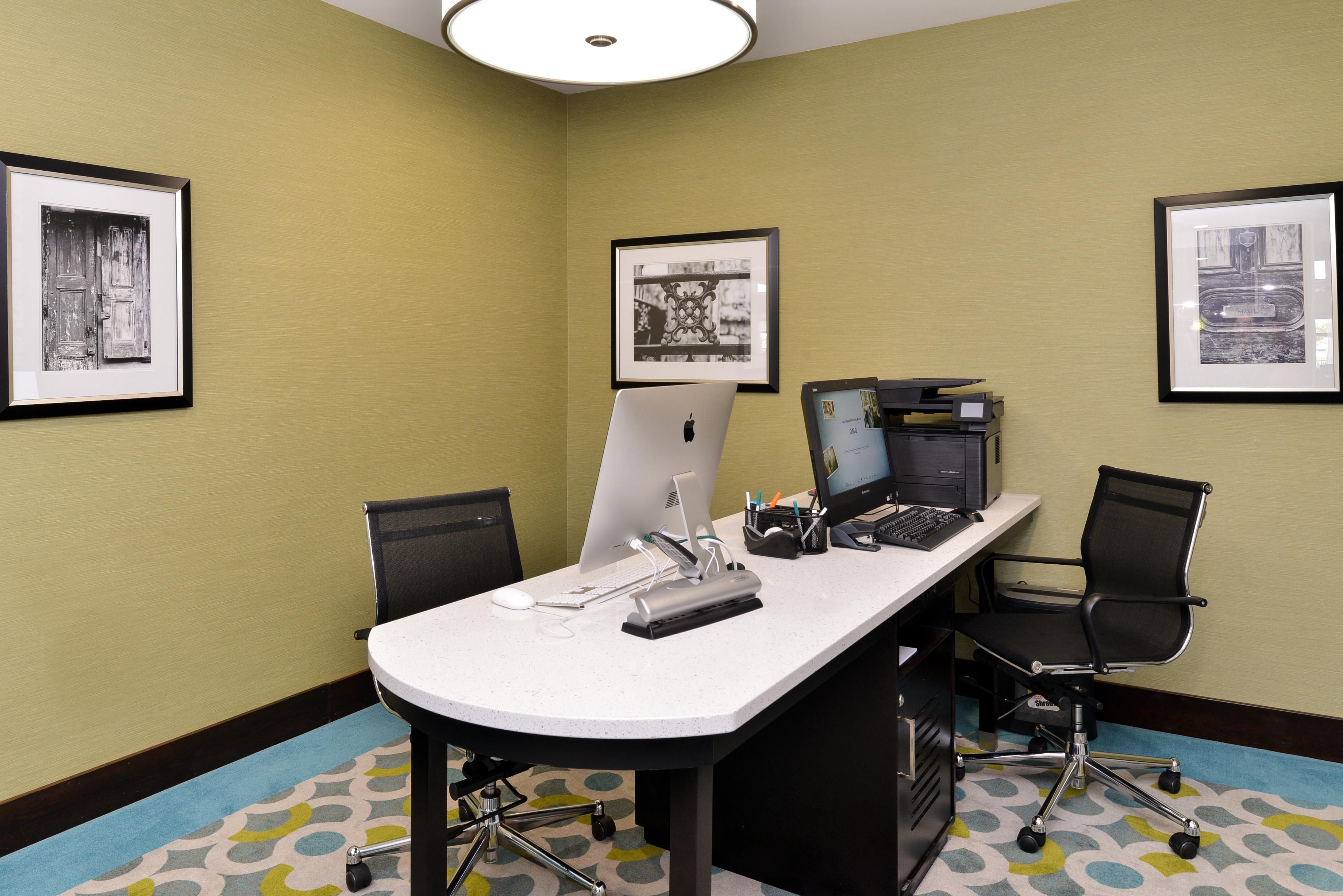 A conference room with a white table, two chairs, a desktop computer, a printer, and framed pictures on the walls.