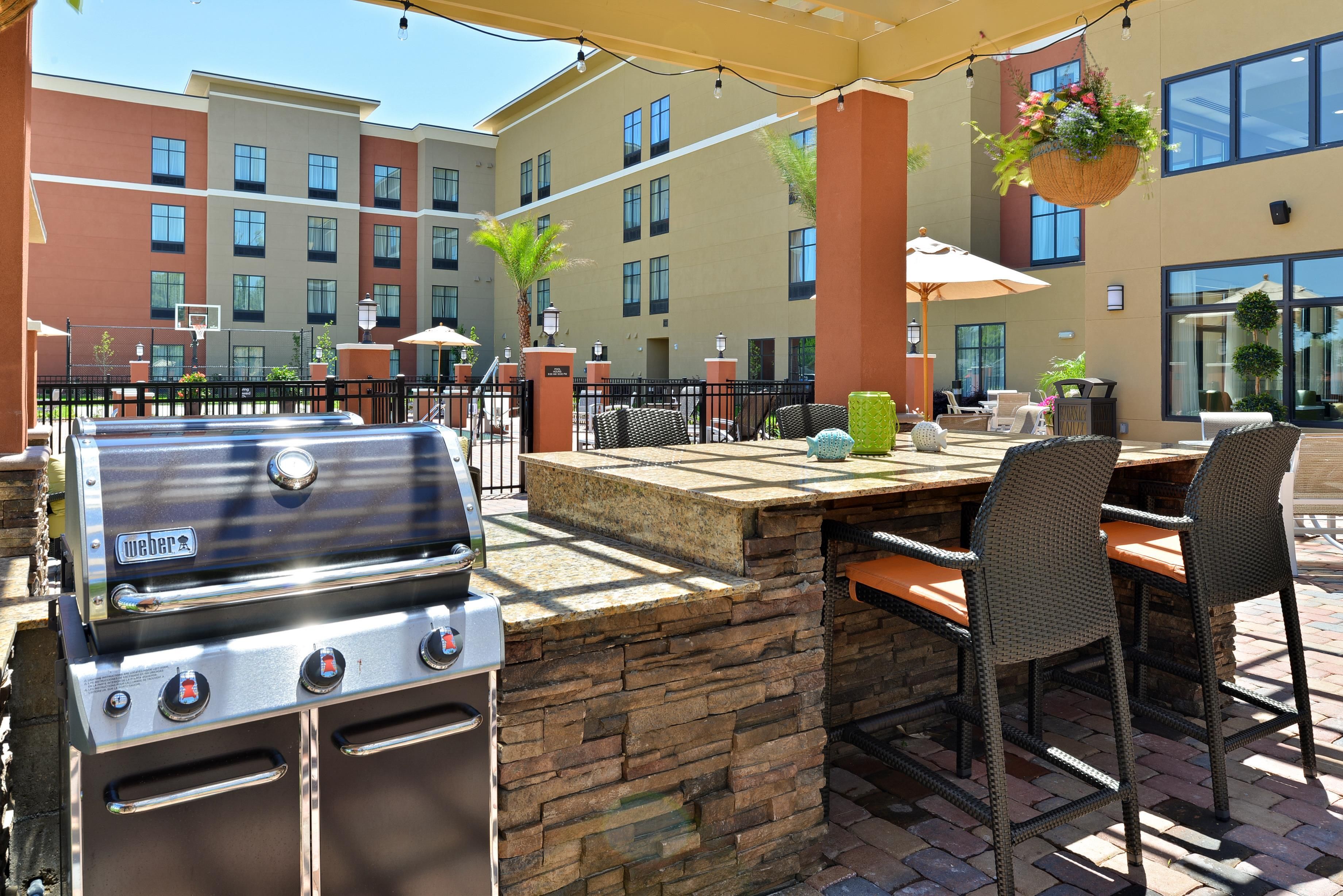 An outdoor patio with a Weber grill, wicker chairs, and a table with a hanging planter.