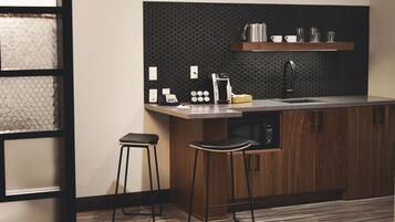 A modern kitchen with wooden cabinets, a black hexagonal backsplash, a stainless steel sink, and two black stools.