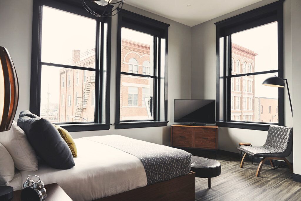 Una camera da letto moderna con un letto grande, una televisione, una sedia e ampie finestre con vista sulla città.