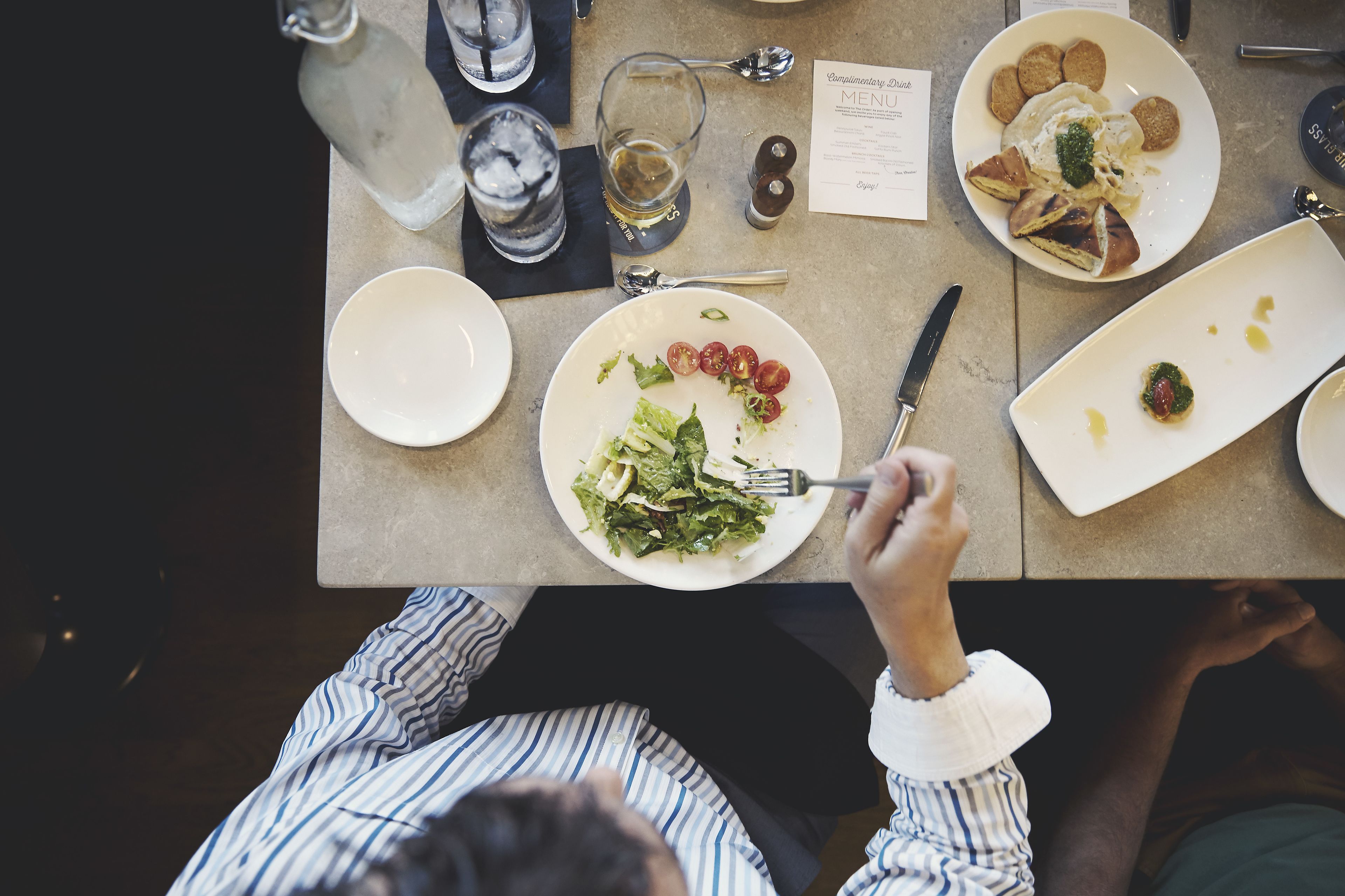 A dining table with plates of food, glasses, and cutlery.
