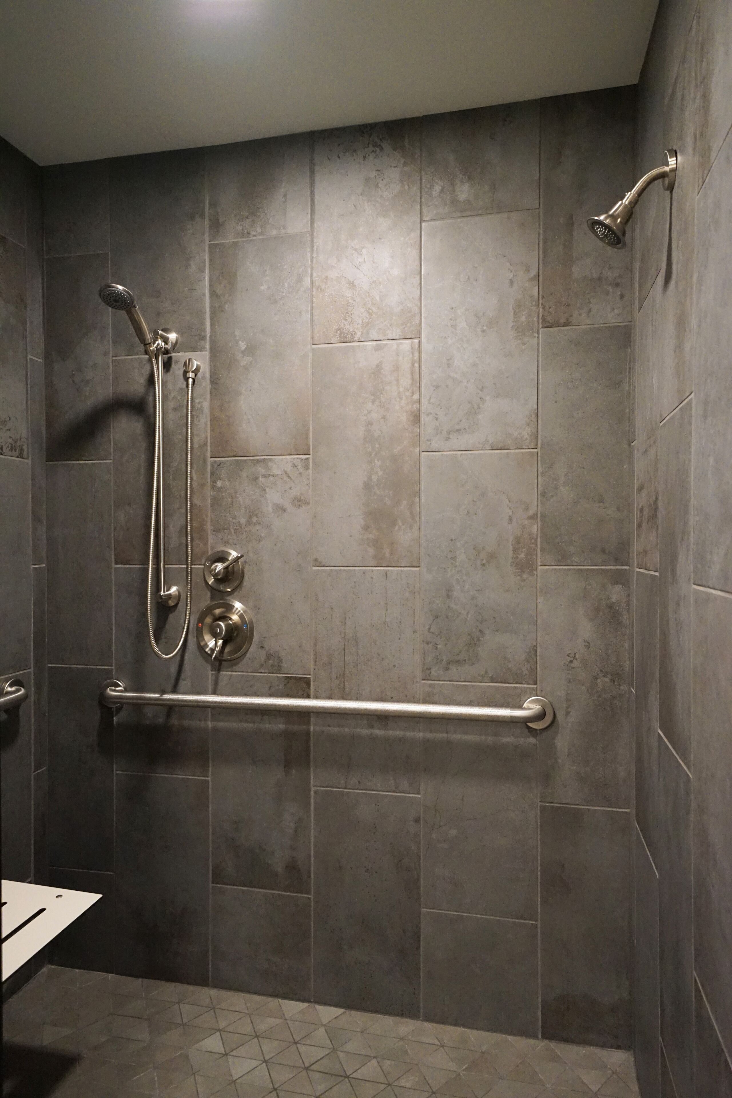 A shower area with a hand shower, a handheld showerhead, and a grab bar.