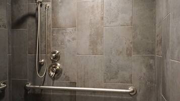 A shower area with a hand shower, a handheld showerhead, and a grab bar.