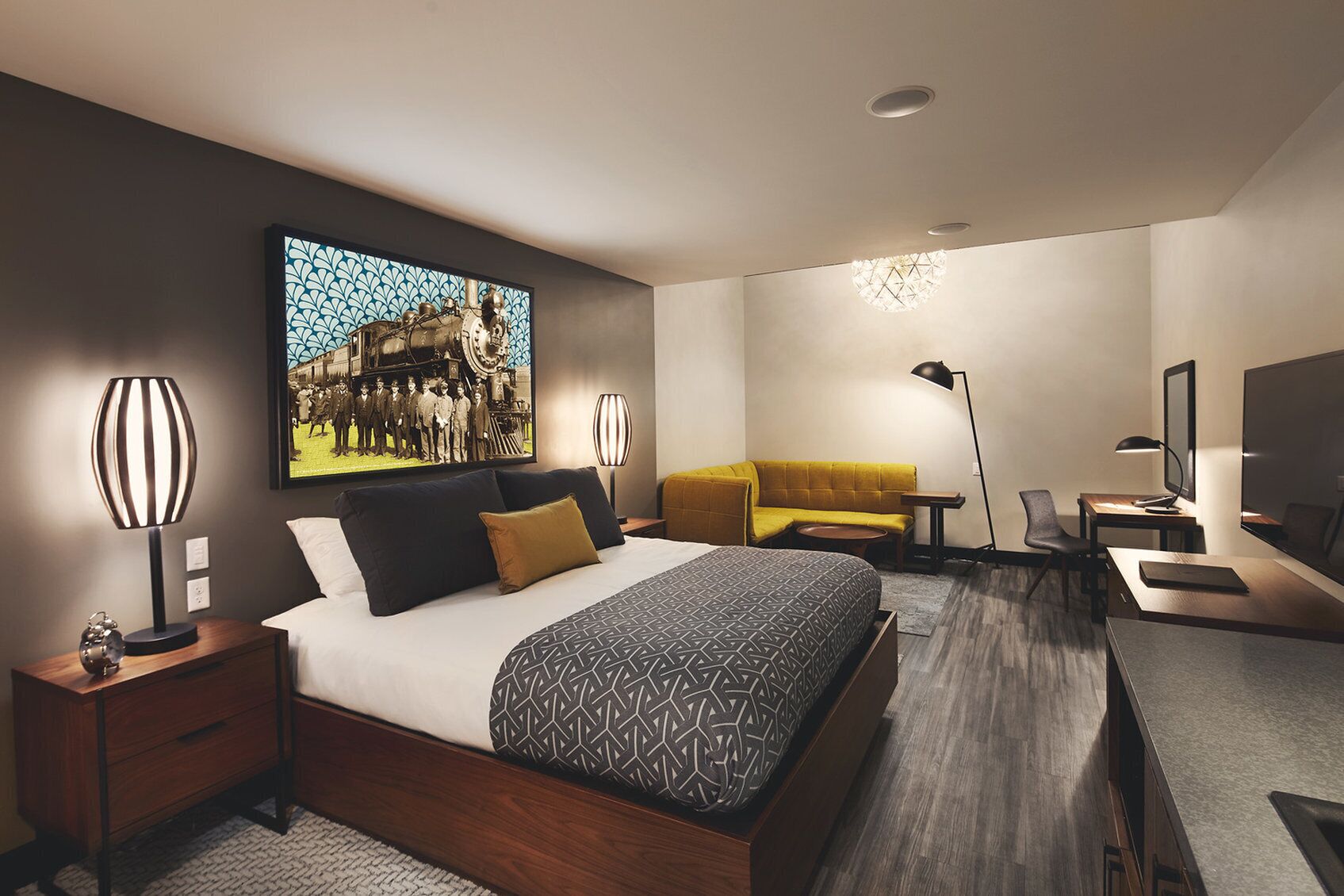 A modern hotel room with a large bed, a sofa, a desk, and a television.