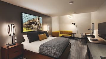 A modern hotel room with a large bed, a sofa, a desk, and a television.