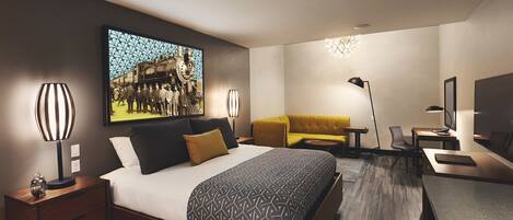 A modern hotel room with a large bed, a sofa, a desk, and a television.
