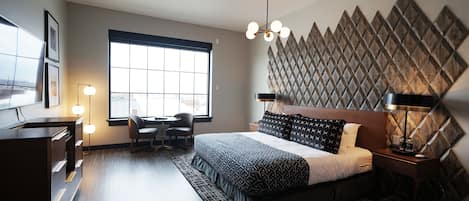 A modern bedroom with a large bed, a desk, and a chair, a window with a view, and a decorative wall panel.
