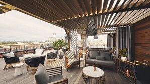 Un lounge en la azotea con suelo de madera, distintas opciones de asientos como sofás y sillas, una mesa redonda y plantas en macetas.