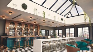Zona de bar con suelo a cuadros, taburetes y una barra larga con estación de barista.