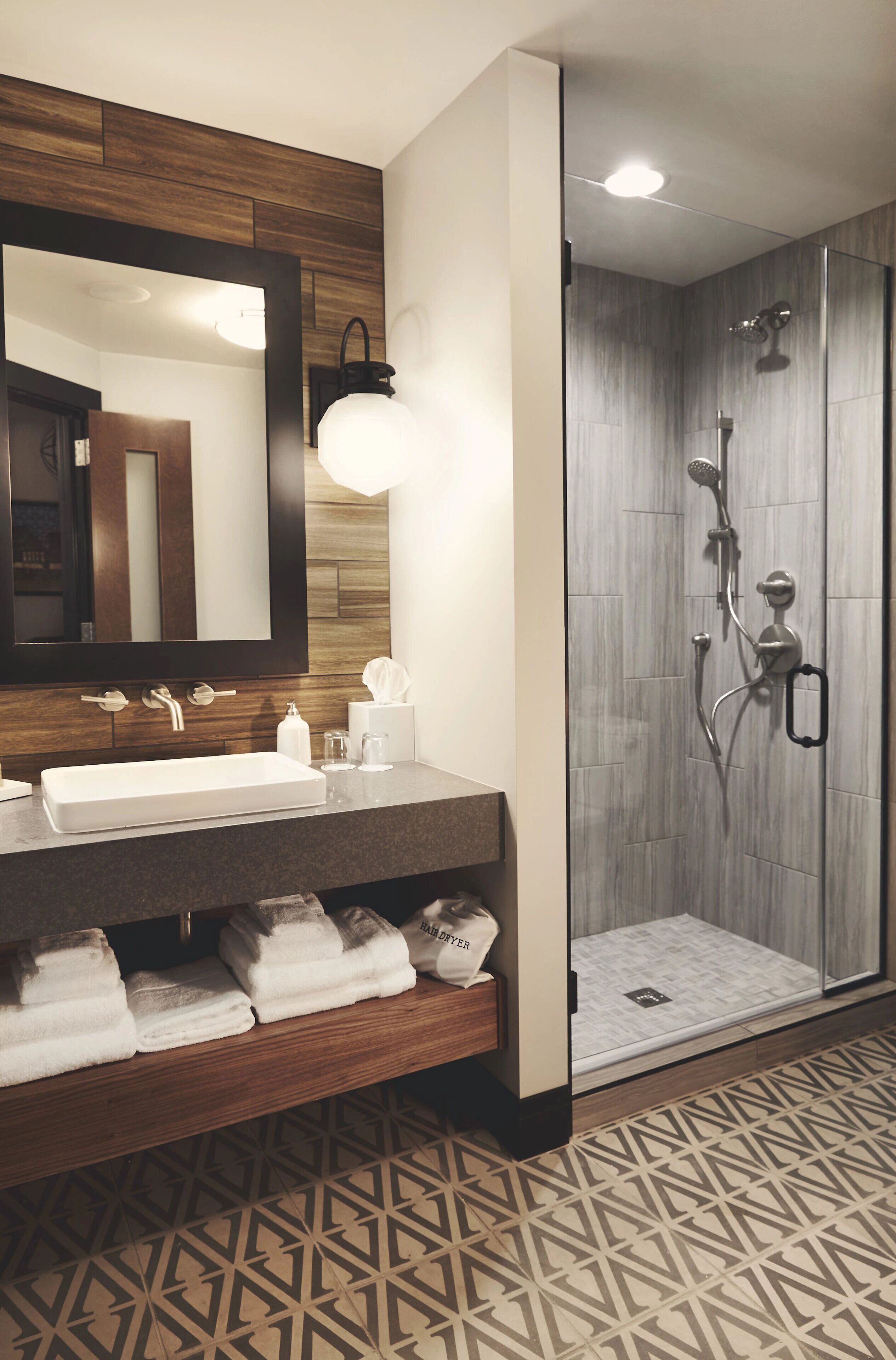Un baño moderno con un espejo grande, un lavabo, una ducha con puerta de cristal y un suelo con diseño.