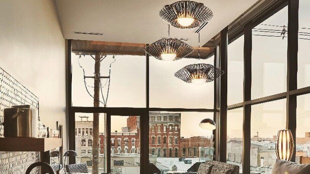 Habitación de hotel moderna con una cama grande, un escritorio con lavabo y vistas a la ciudad a través de amplios ventanales.