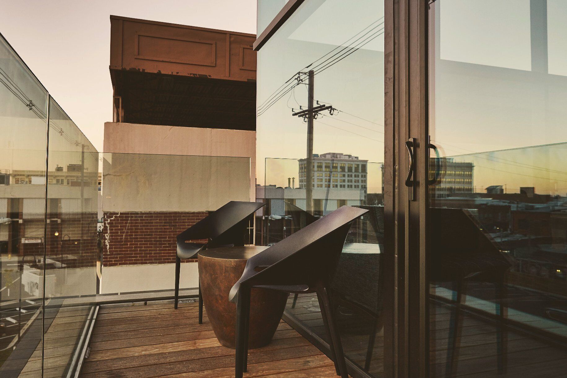 A modern balcony with a glass railing, a metal chair, and a large planter.
