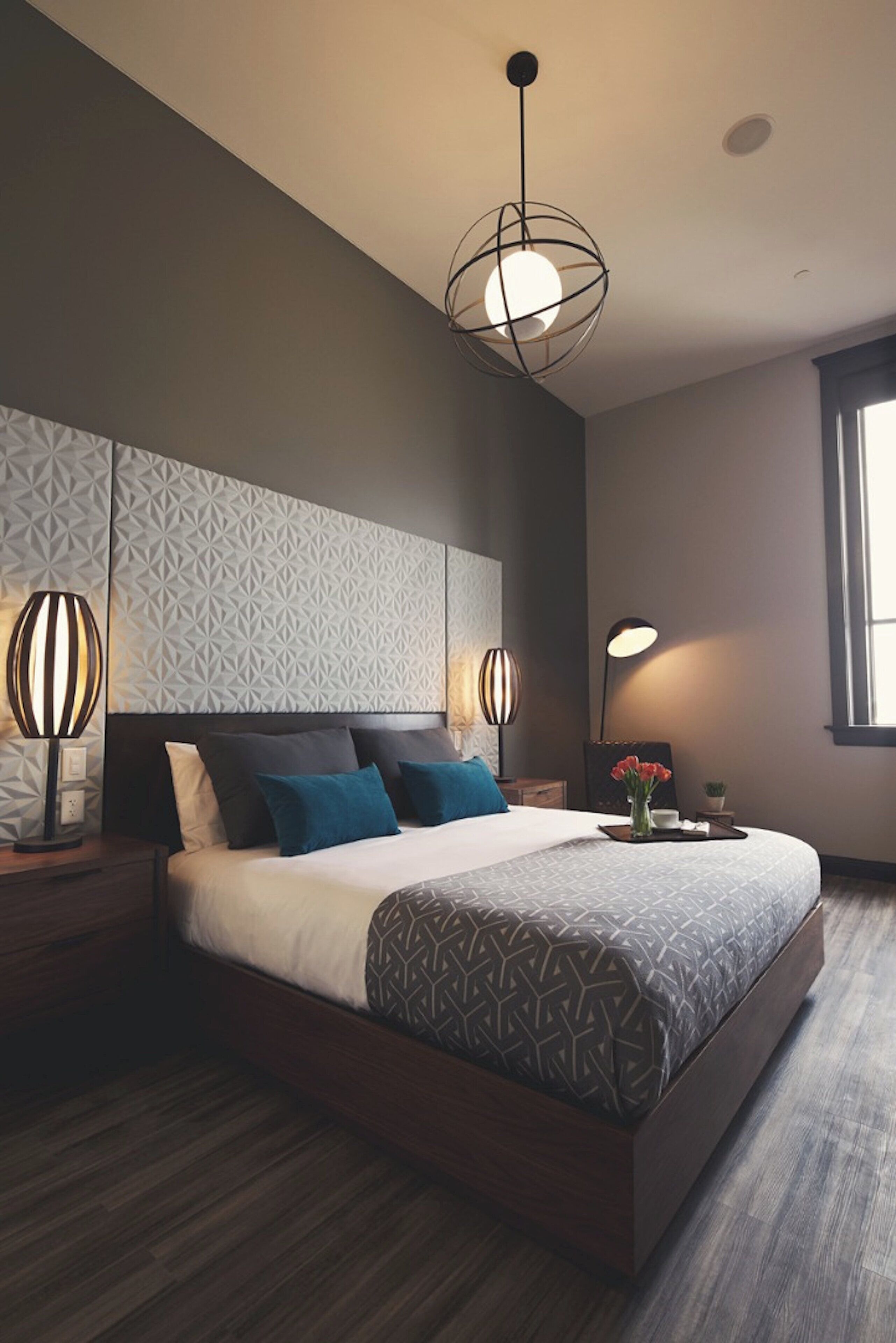 Un dormitorio moderno con una cama grande, cabecera con estampado geométrico, dos lámparas de noche y una ventana con luz natural.