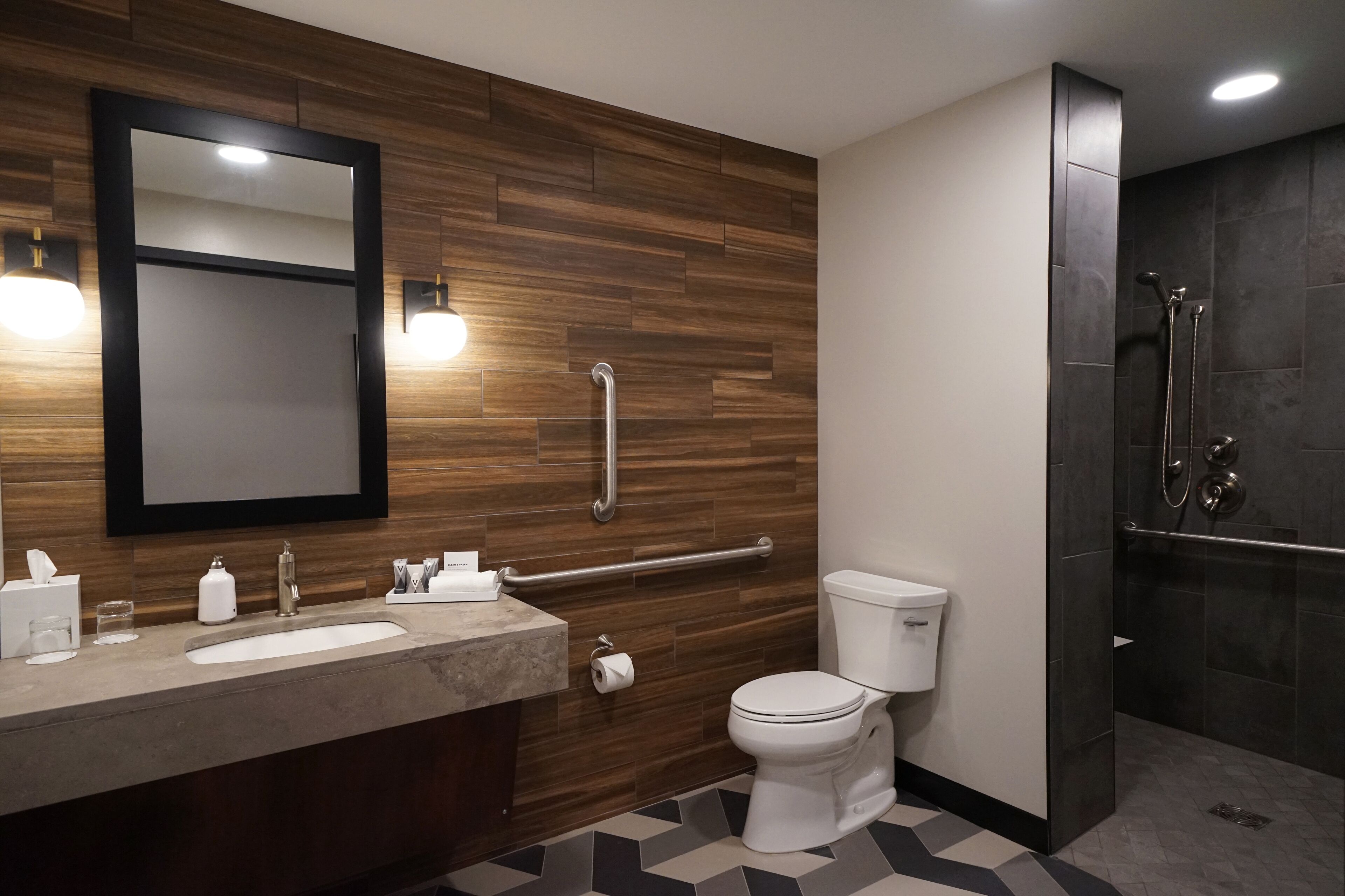 Een moderne badkamer met een houten wand, een grote spiegel, een wastafel met twee kommen, een toilet en een douchehoek.