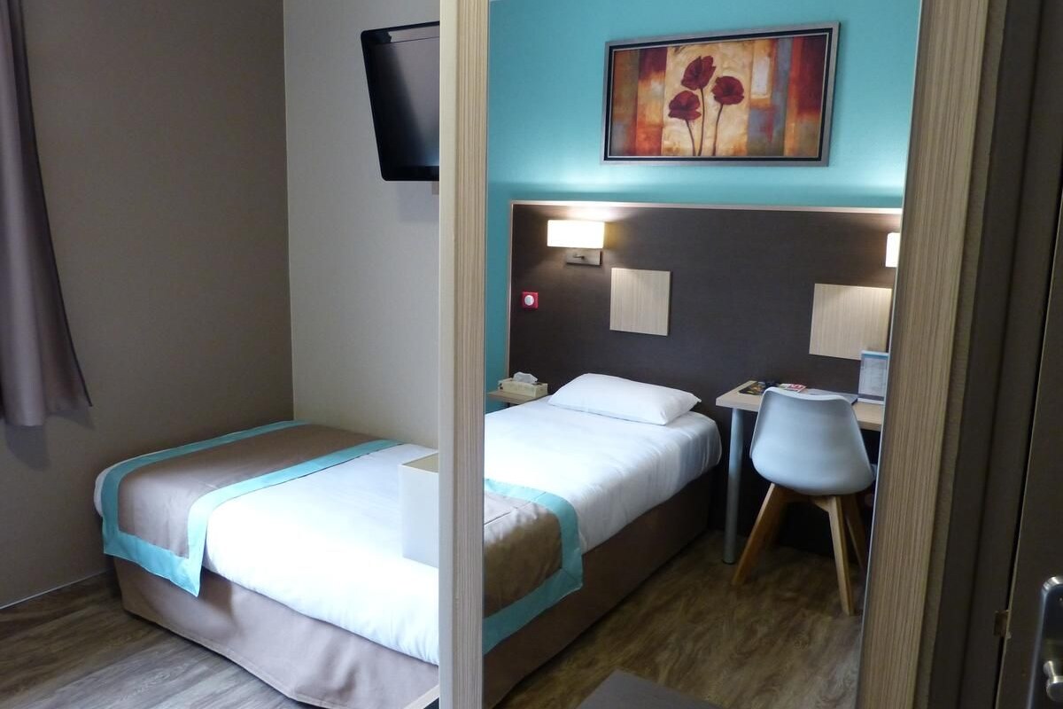 Habitación de hotel compacta con dos camas, un escritorio, una silla y un televisor montado en la pared.