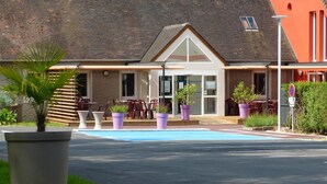 A building with a tiled roof, a covered patio with outdoor seating, and a swimming pool. - Hôtel Arbor (Mulsanne)