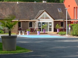 A building with a tiled roof, a covered patio with outdoor seating, and a swimming pool.