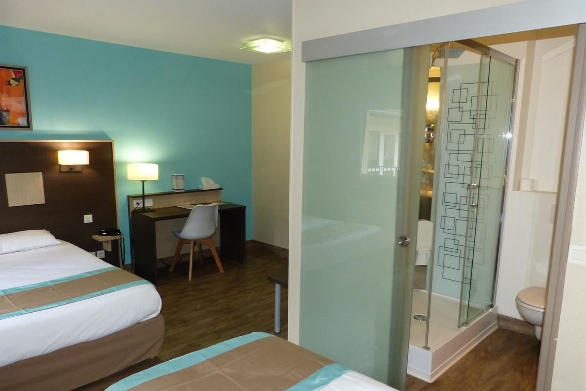 A hotel room with two beds, a desk, a chair, and a shower area.