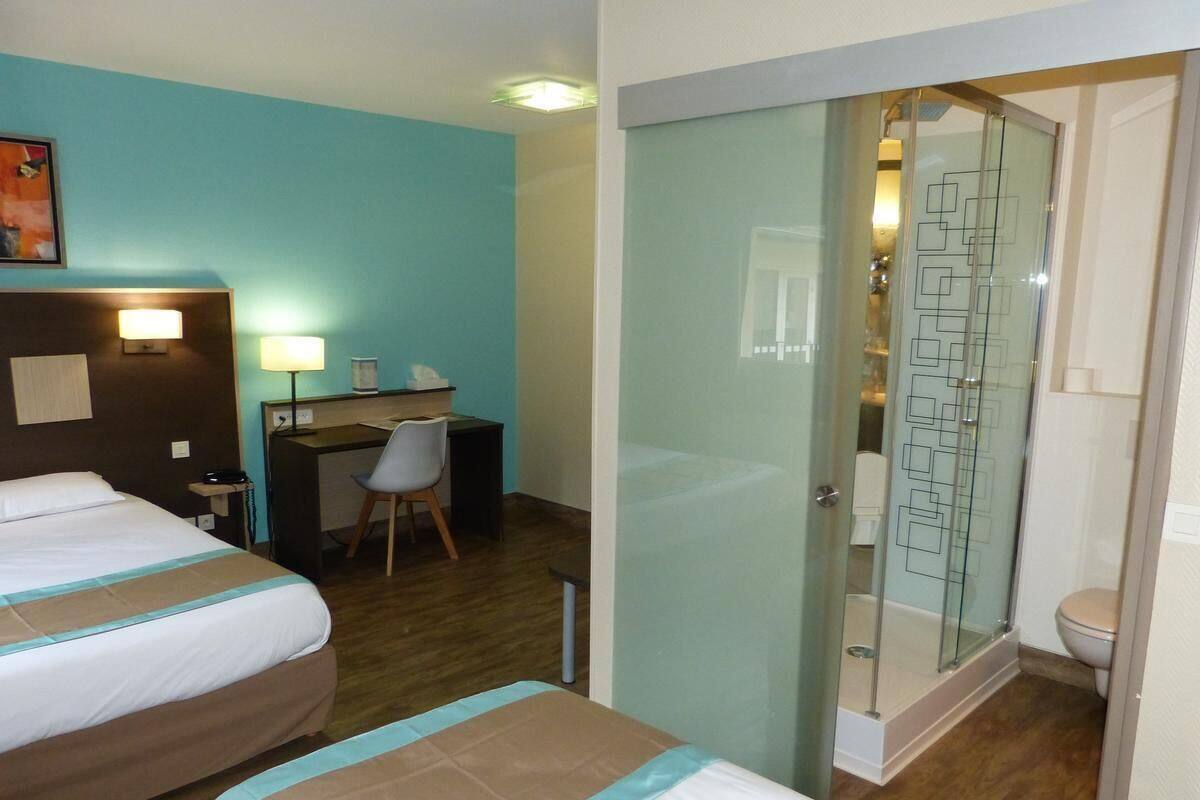 A hotel room with two beds, a desk, a chair, and a shower area.
