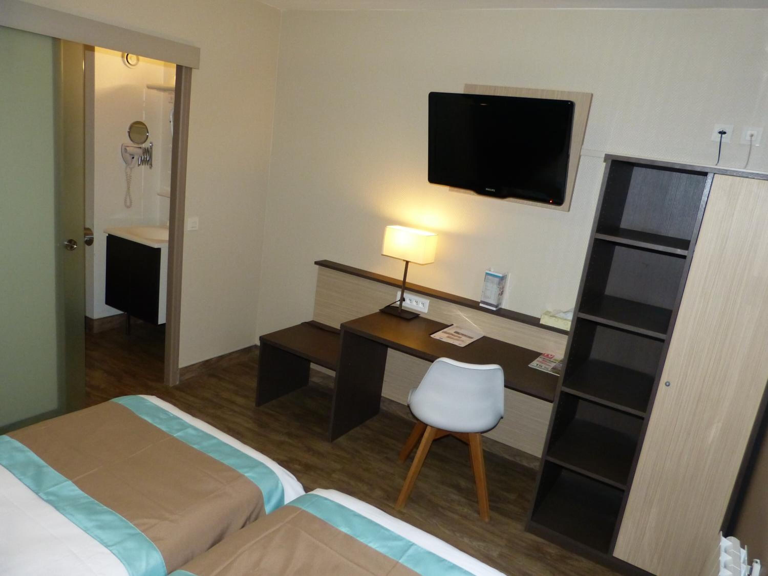 A hotel room with two beds, a desk with a chair, a television, and a wardrobe.