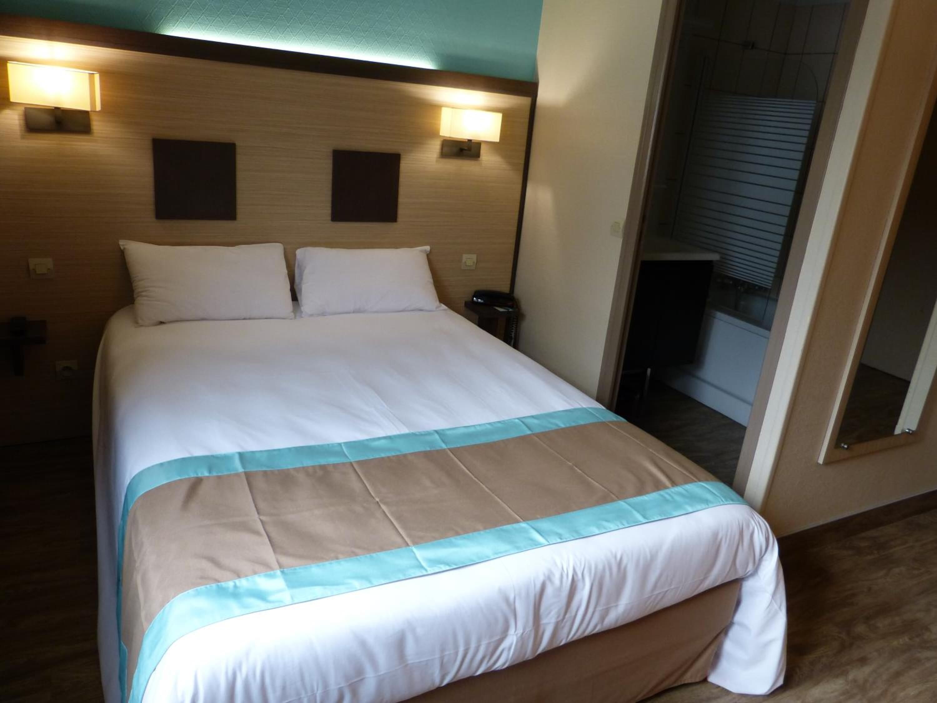 Een hotelkamer met een groot bed, twee bedlampen en een spiegel aan de muur.