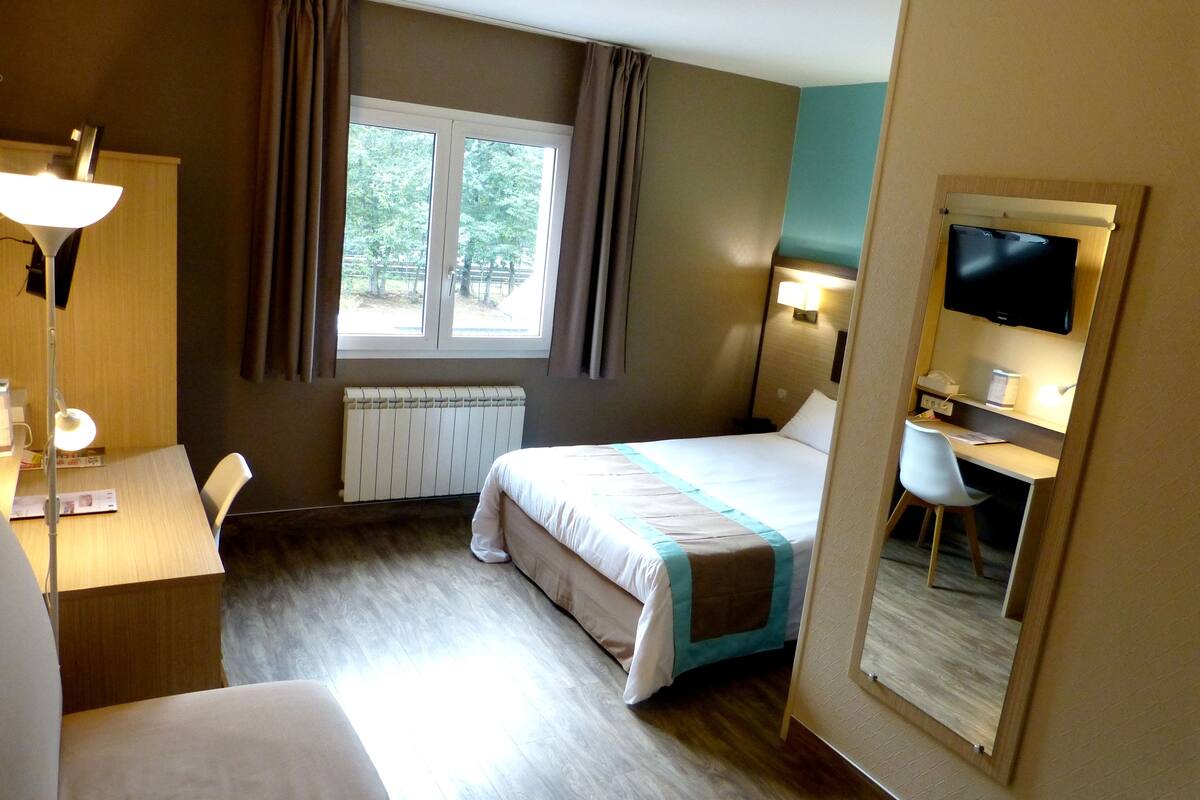 A hotel room with a bed, desk, chair, and a TV.
