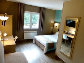 A hotel room with a bed, desk, chair, and a TV.