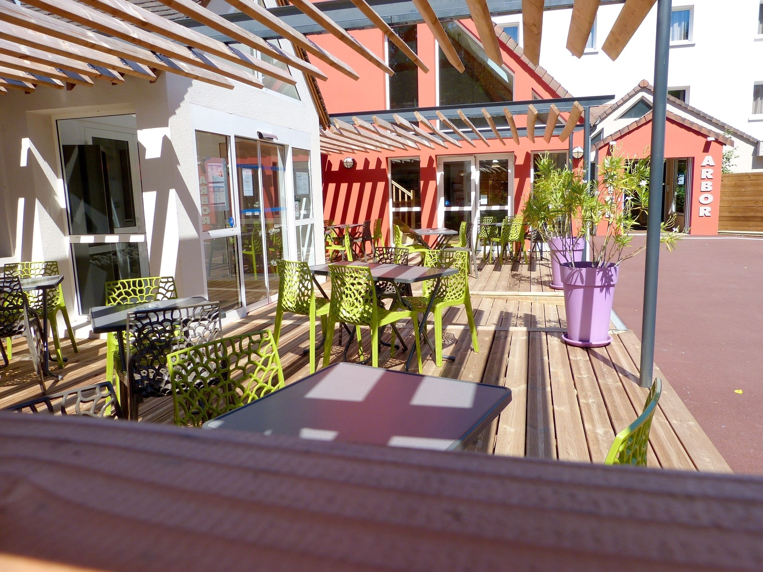 Een terras met tafels en stoelen, een houten terras en een gebouw met een rood-witte gevel.