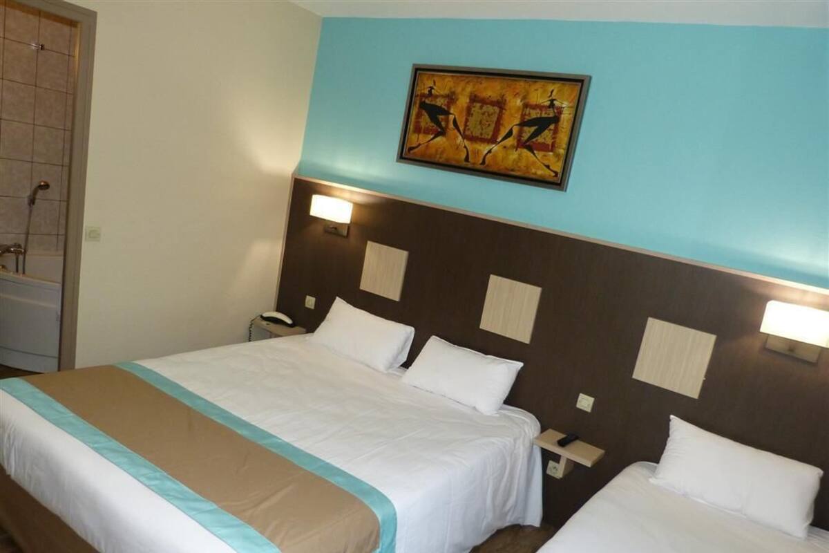 A hotel room with two beds, a painting on the wall, and a nightstand with a lamp.