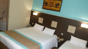 A hotel room with two beds, a painting on the wall, and a nightstand with a lamp.