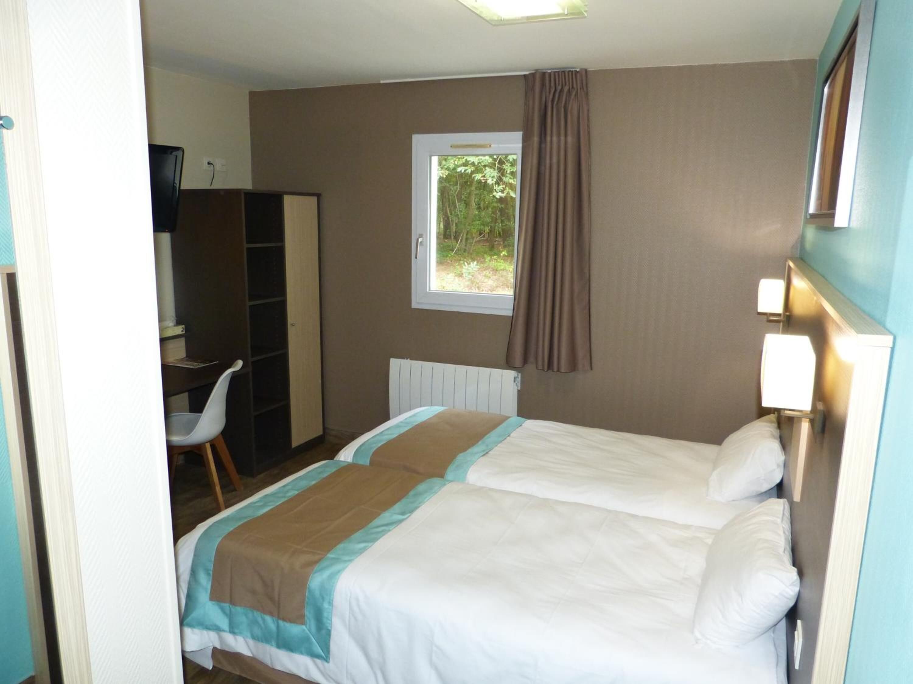 Ett hotellrum med två sängar, ett skrivbord, en garderob och ett fönster med gardiner.