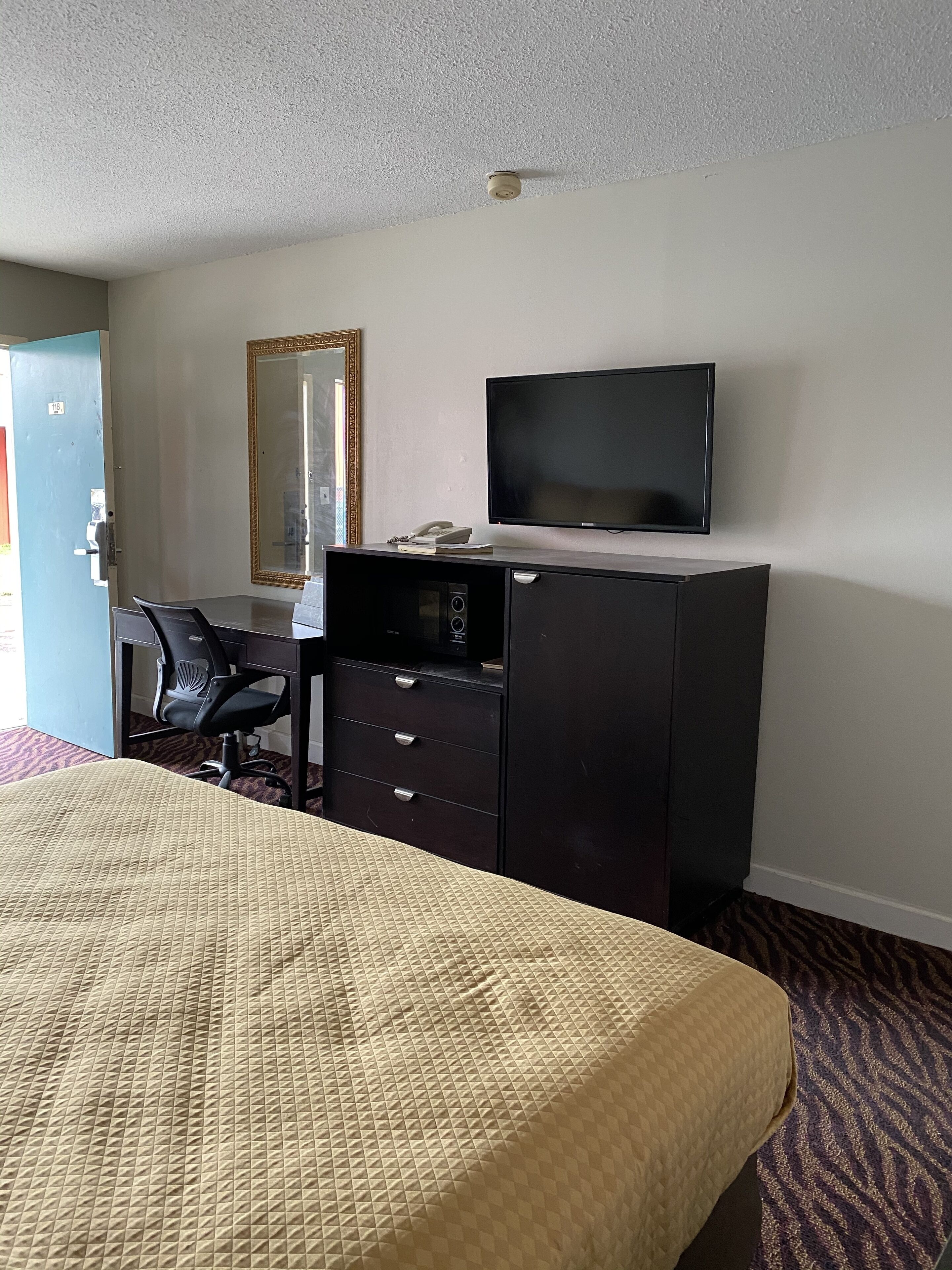 Een hotelkamer met een bed, een bureau met stoel, een televisie, een kast en een spiegel.