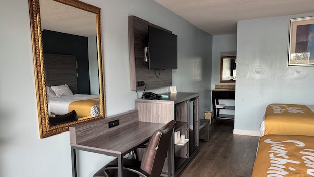 A hotel room with a bed, a desk with a chair, a mirror, a television, and a bedside table. - Red Carpet Inn & Suites (Danville)