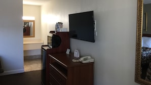 A hotel room with a flat-screen TV mounted on the wall, a wooden desk with a telephone, and a mirror with an ornate frame. - Red Carpet Inn & Suites (Danville)