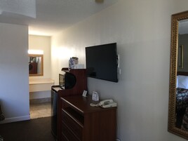 Quarto de hotel com televisão de tela plana na parede, escrivaninha de madeira com telefone e espelho com moldura ornamentada.