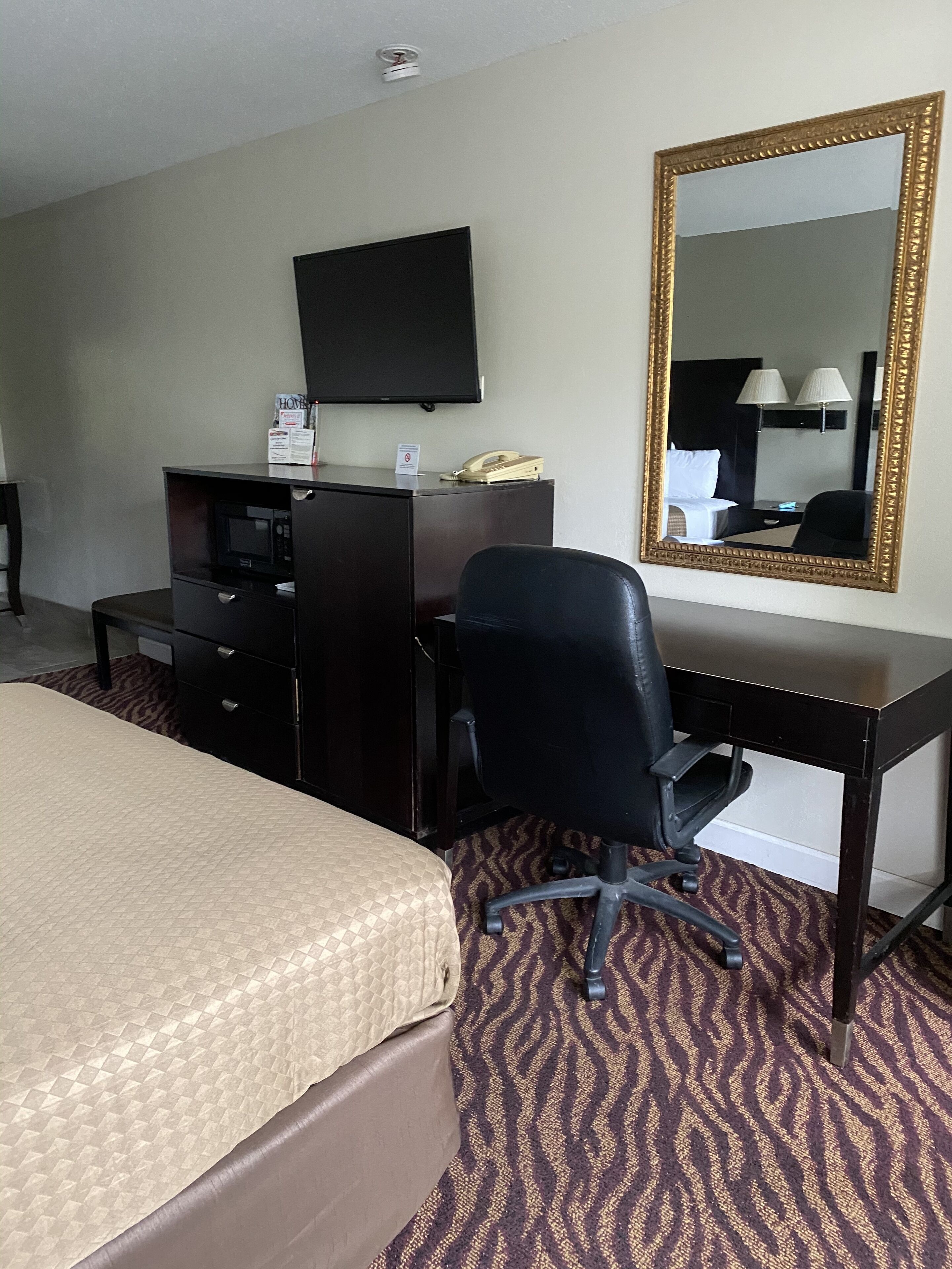 Habitación de hotel con cama, escritorio, silla, televisión, teléfono y espejo.