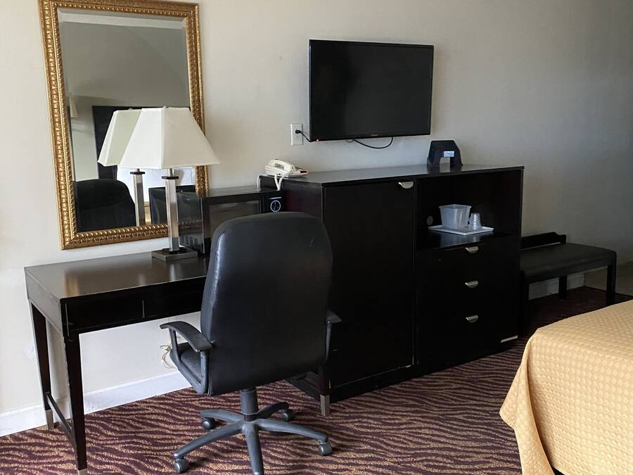 A hotel room with a desk, chair, television, and a bed.