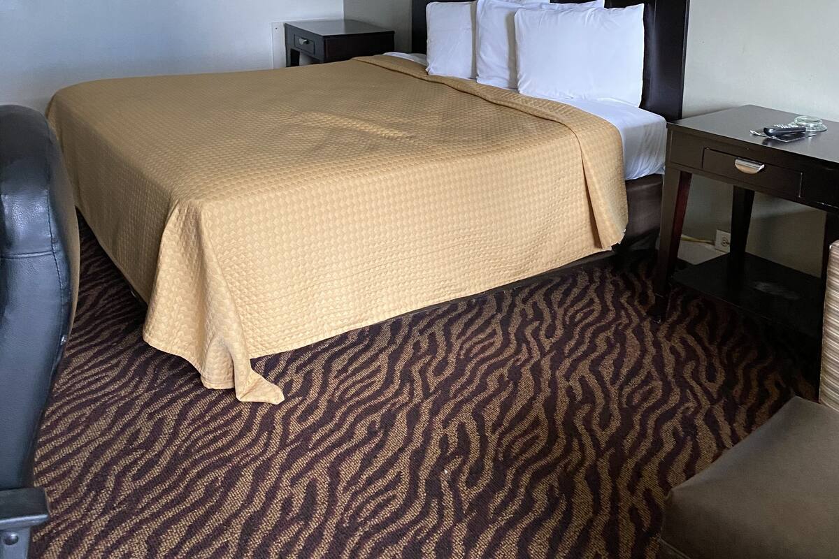 A hotel room with a bed, a desk, a chair, and a lamp.
