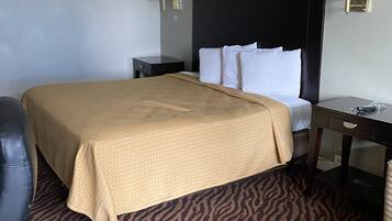 A hotel room with a bed, a desk, a chair, and a lamp.
