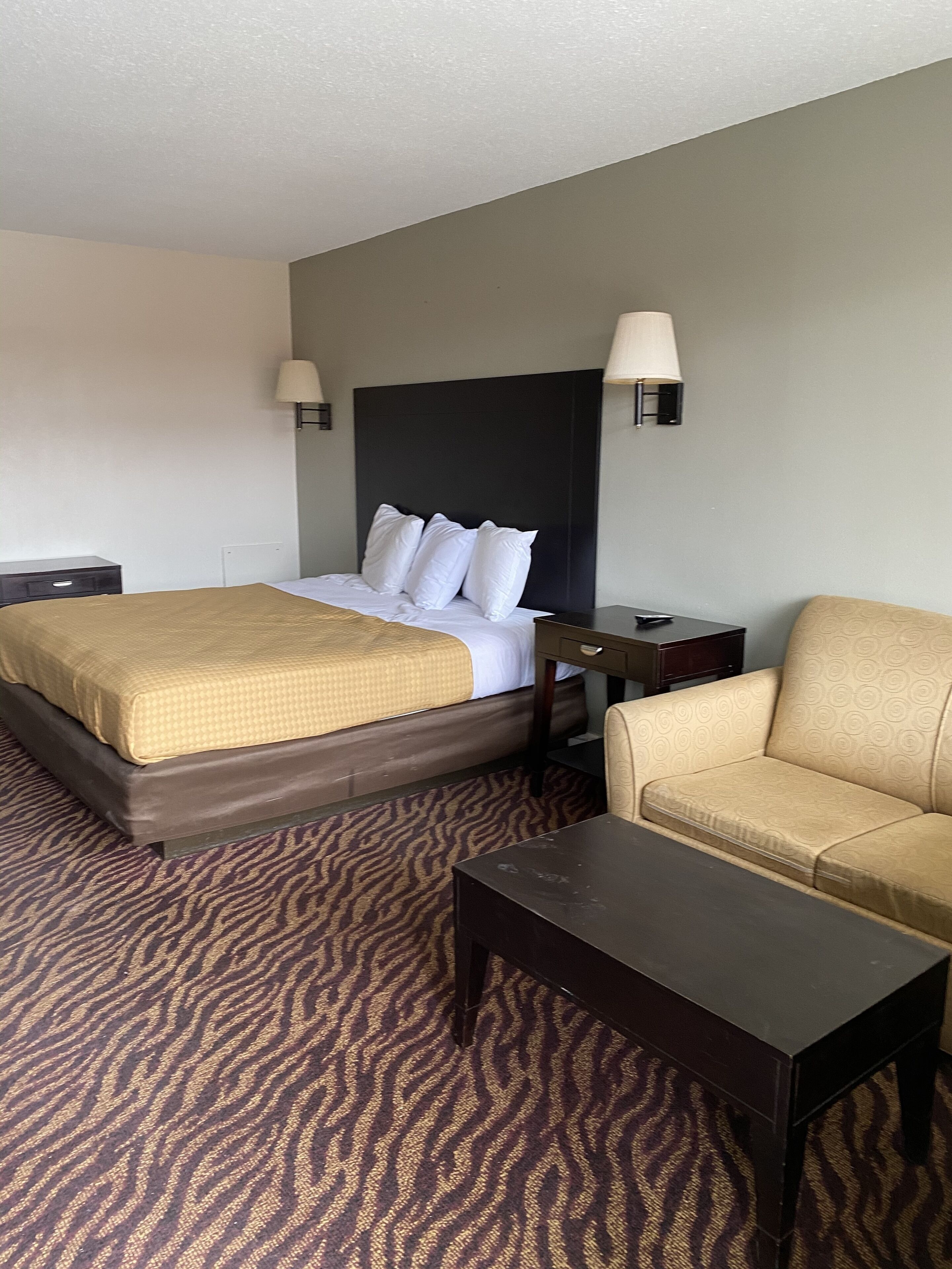 Une chambre d’hôtel avec un lit, un canapé, une petite table et deux lampes fixées au mur.