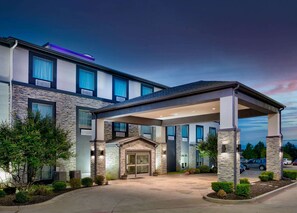 A modern hotel with a covered entrance, stone facade, and multiple windows.