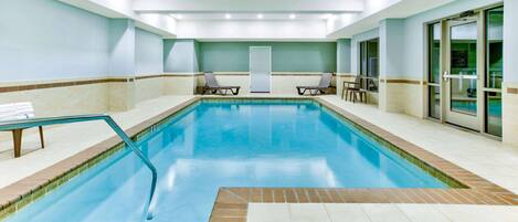 Una amplia piscina interior con agua cristalina, rodeada de sillones de descanso y un suelo de baldosas.