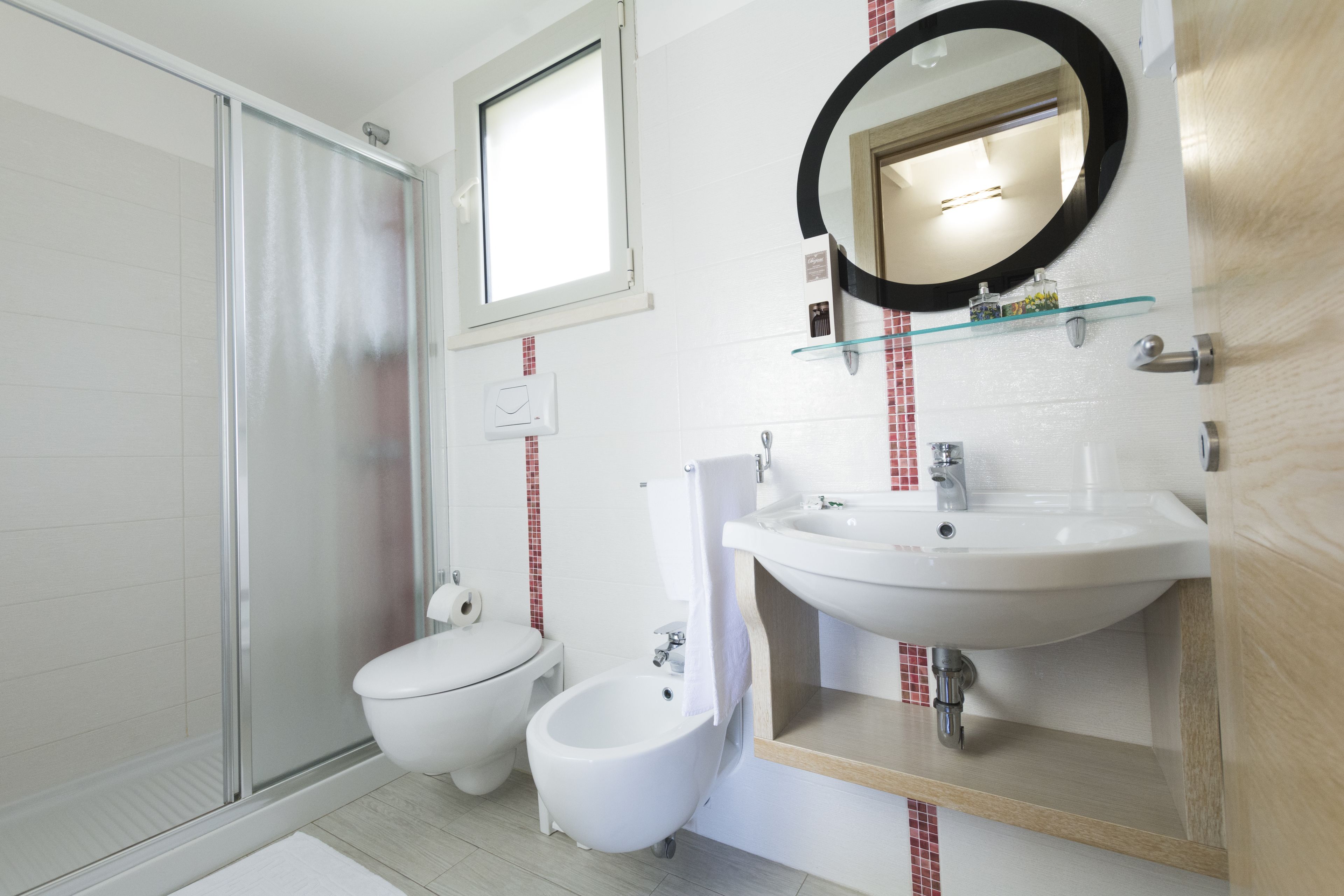 A modern bathroom with a glass shower enclosure, a toilet, a bidet, and a sink with a mirror above it.
