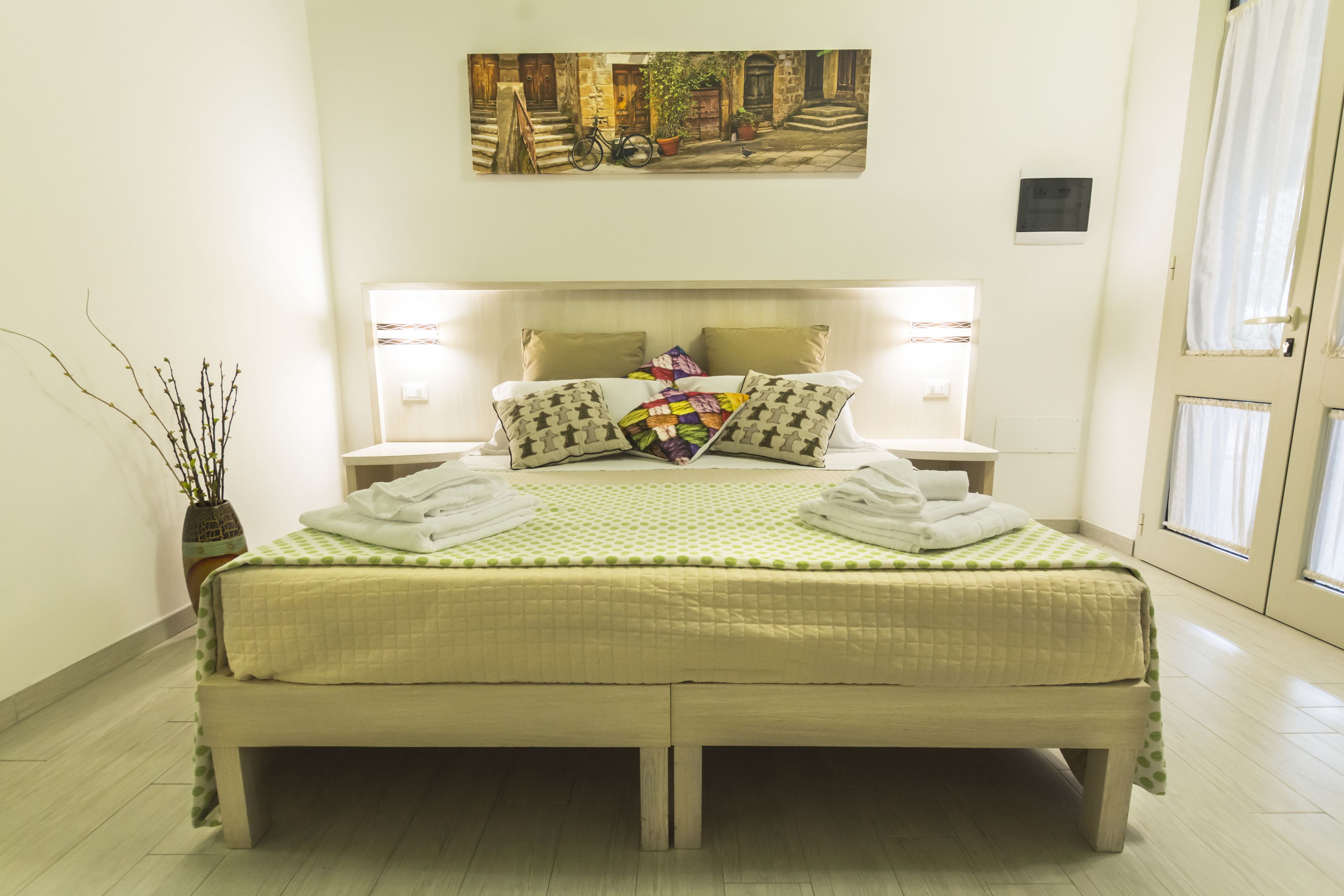 A neatly made bed with a quilted green and white bedspread, two pillows, and two folded towels.