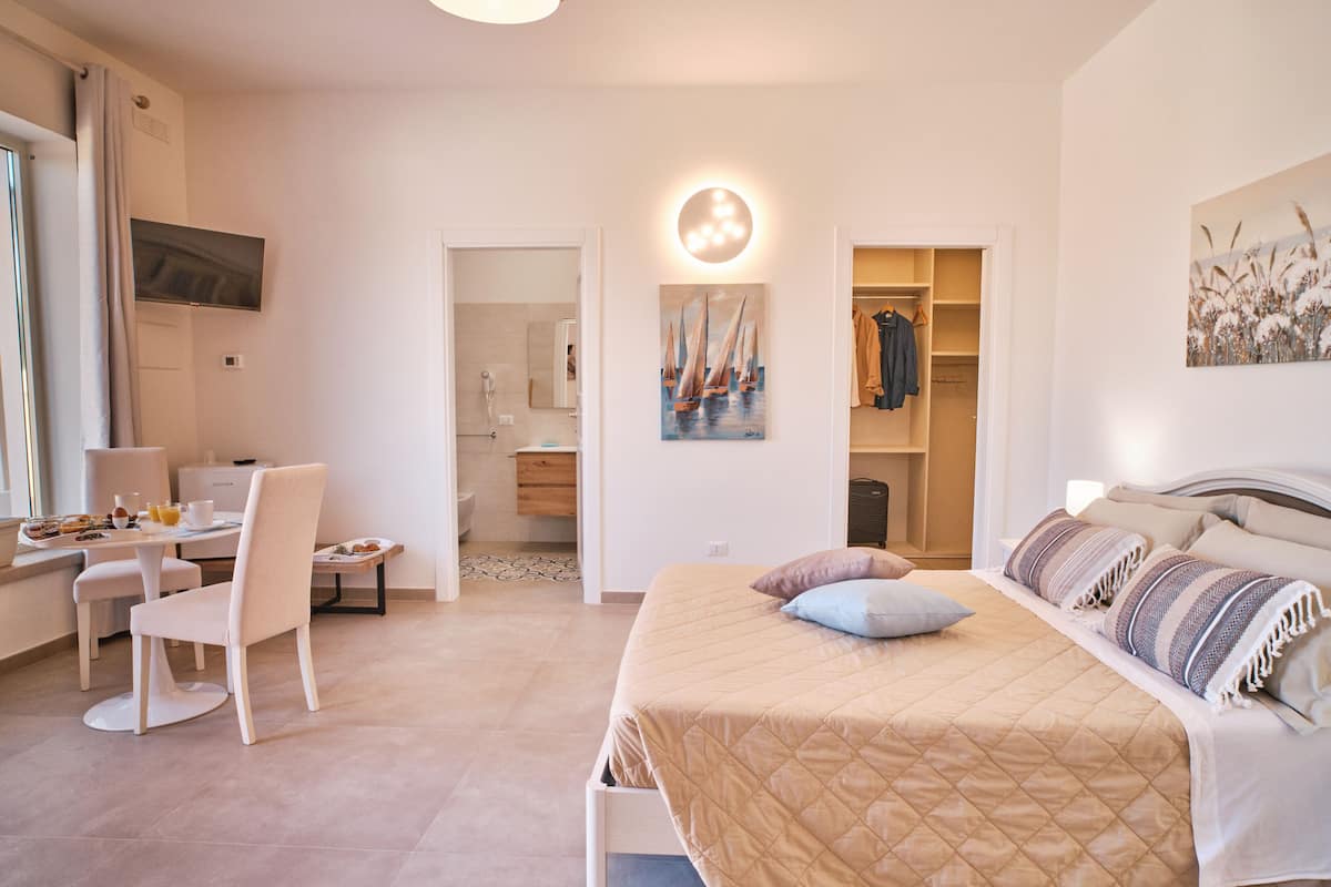 A modern hotel room with a bed, a desk, and a chair. There is a bathroom visible through an open door.