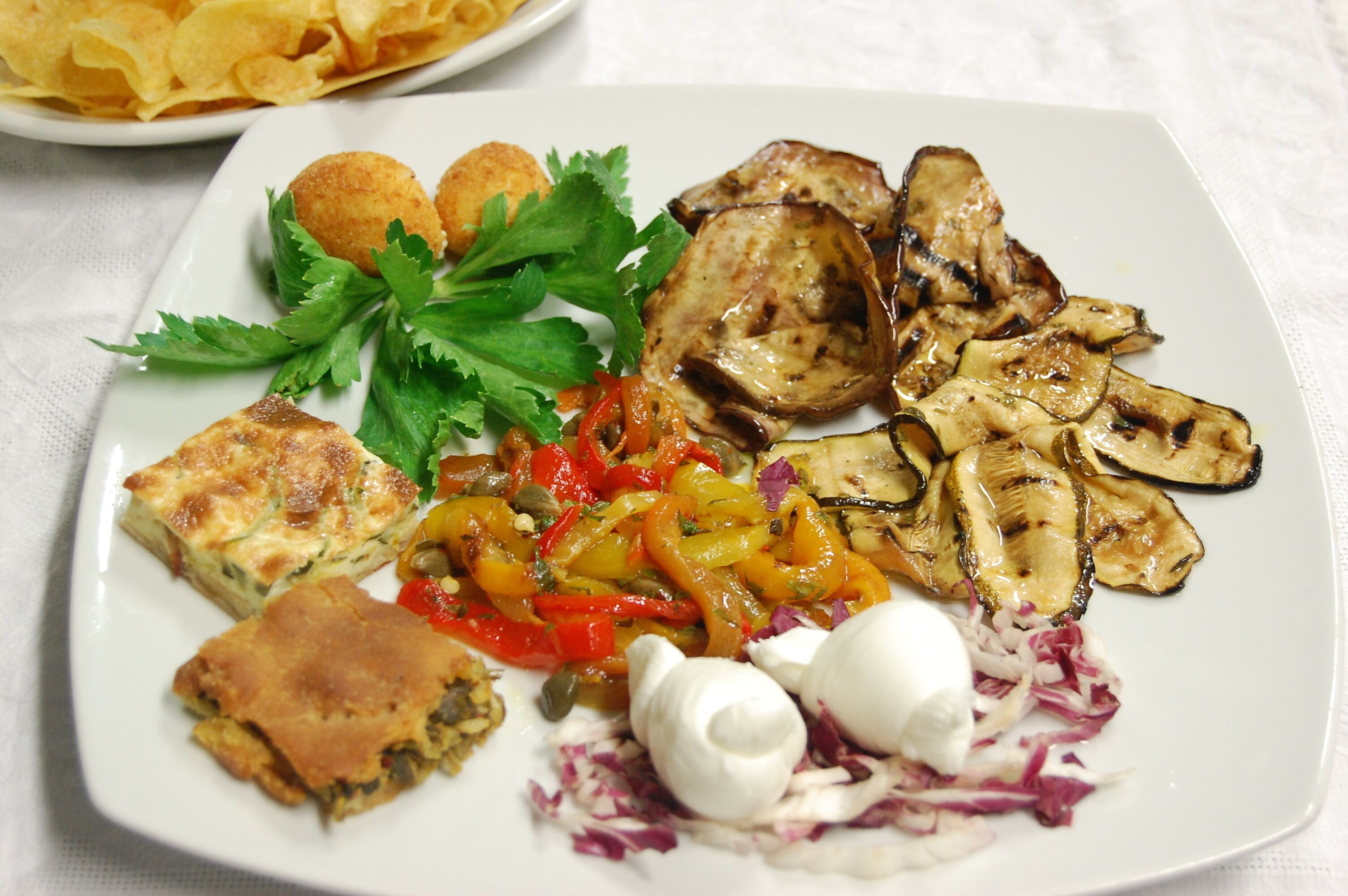 A plate of food with grilled vegetables, a slice of pie, and a side of chips.