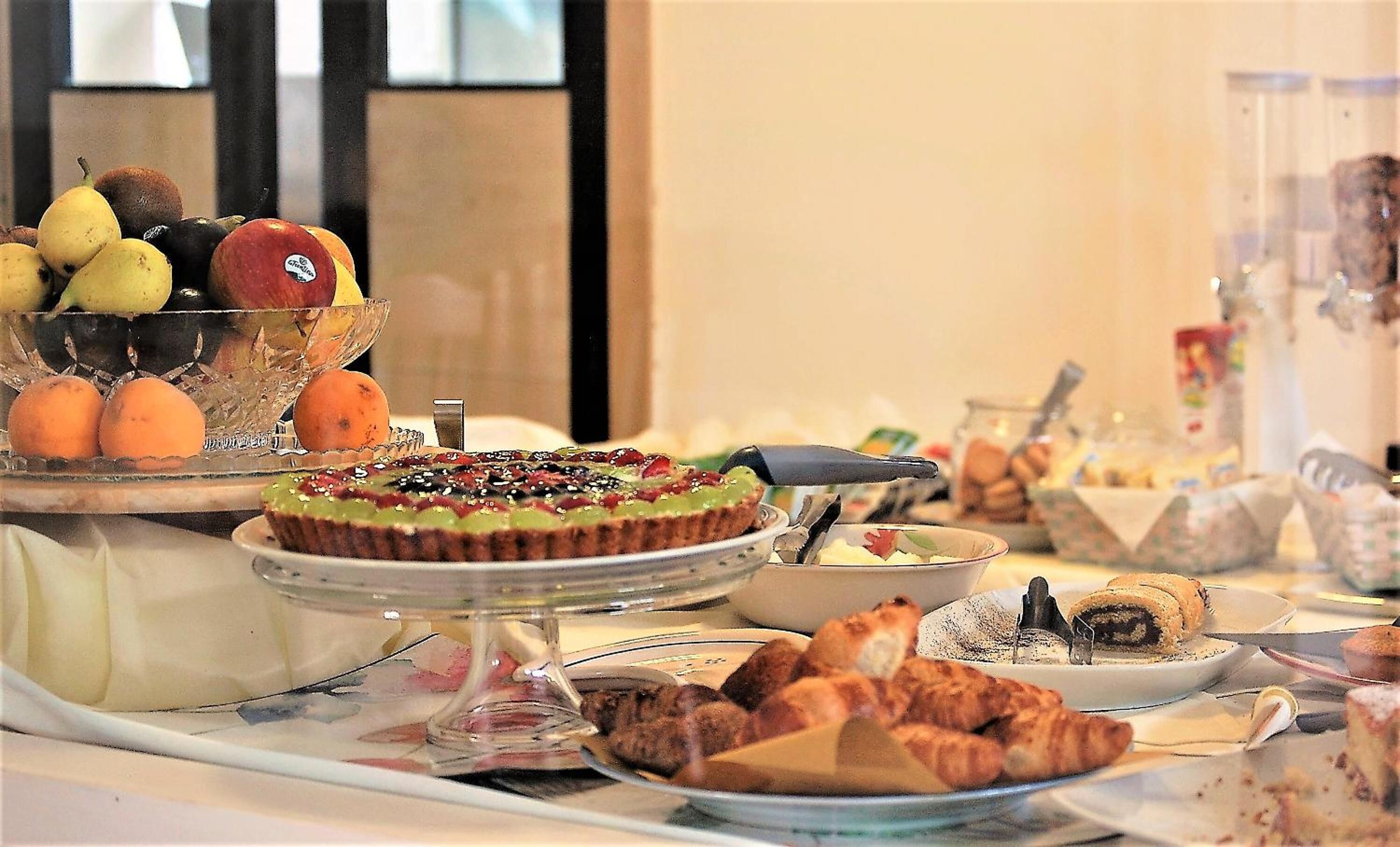 Ein Buffet mit verschiedenen Speisen, darunter eine Obstschale, eine dekorierte Torte, Gebäck und ein Fleischgericht.